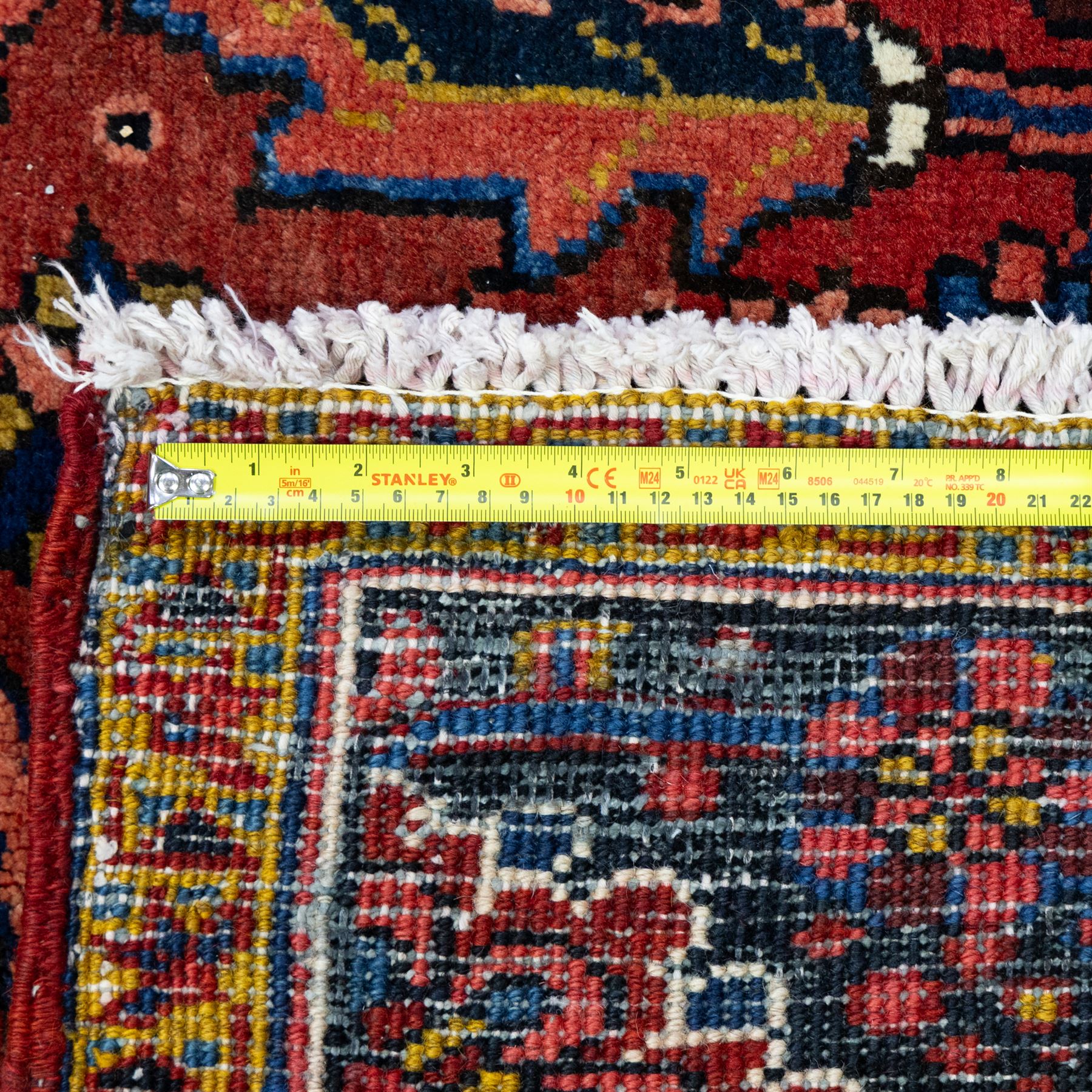 North West Persian Ahar hand-knotted carpet, madder red ground, with a large central shaped floral medallion with pendants, surrounded by angular scrolling foliate motifs incorporating rosettes, palmettes and stylised flowerheads, enclosed by ivory spandrels and a dark navy border with repeating floral motifs and meandering vines, flanked by narrow floral guard stripes, with cotton fringes