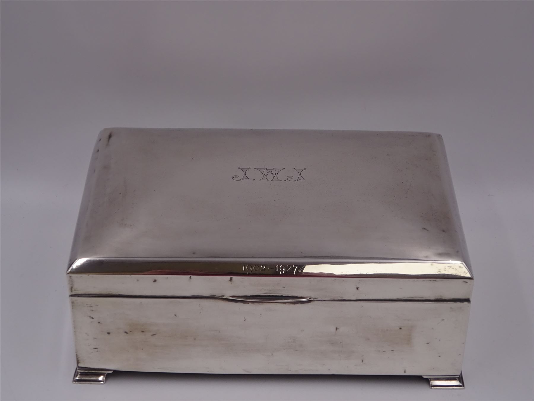 1920s silver mounted presentation cigarette box, of rectangular form, with engraved initials J.W.J and dated 1902-1927 to slightly domed hinged cover, opening to reveal compartmentalised softwood interior, upon four bracket feet, hallmarked Birmingham 1920, maker's mark worn and indistinct, H9cm, W23cm, reputedly given to John William Johnson, father of Amy Johnson,  famous for being the first long distance (to Australia) solo female pilot, and first female British grounds engineer, for his silver wedding anniversary