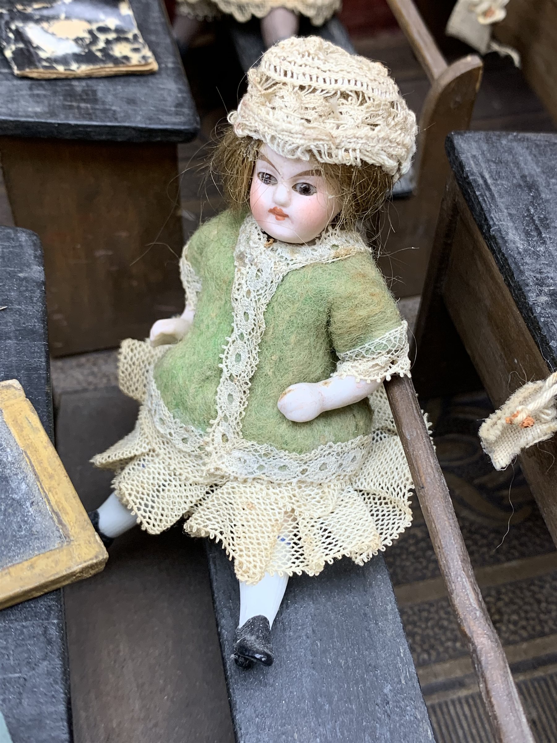 Late Victorian wooden school room setting with bisque head teacher and six German all bisque pupils each seated at a combined desk and chair with slate board, in a classroom furnished with chest of drawers, fire-surround, lectern, wall map, pictures, miniature books, school bell, chalk board on easel, wall clock etc, L70cm H28cm D28cm