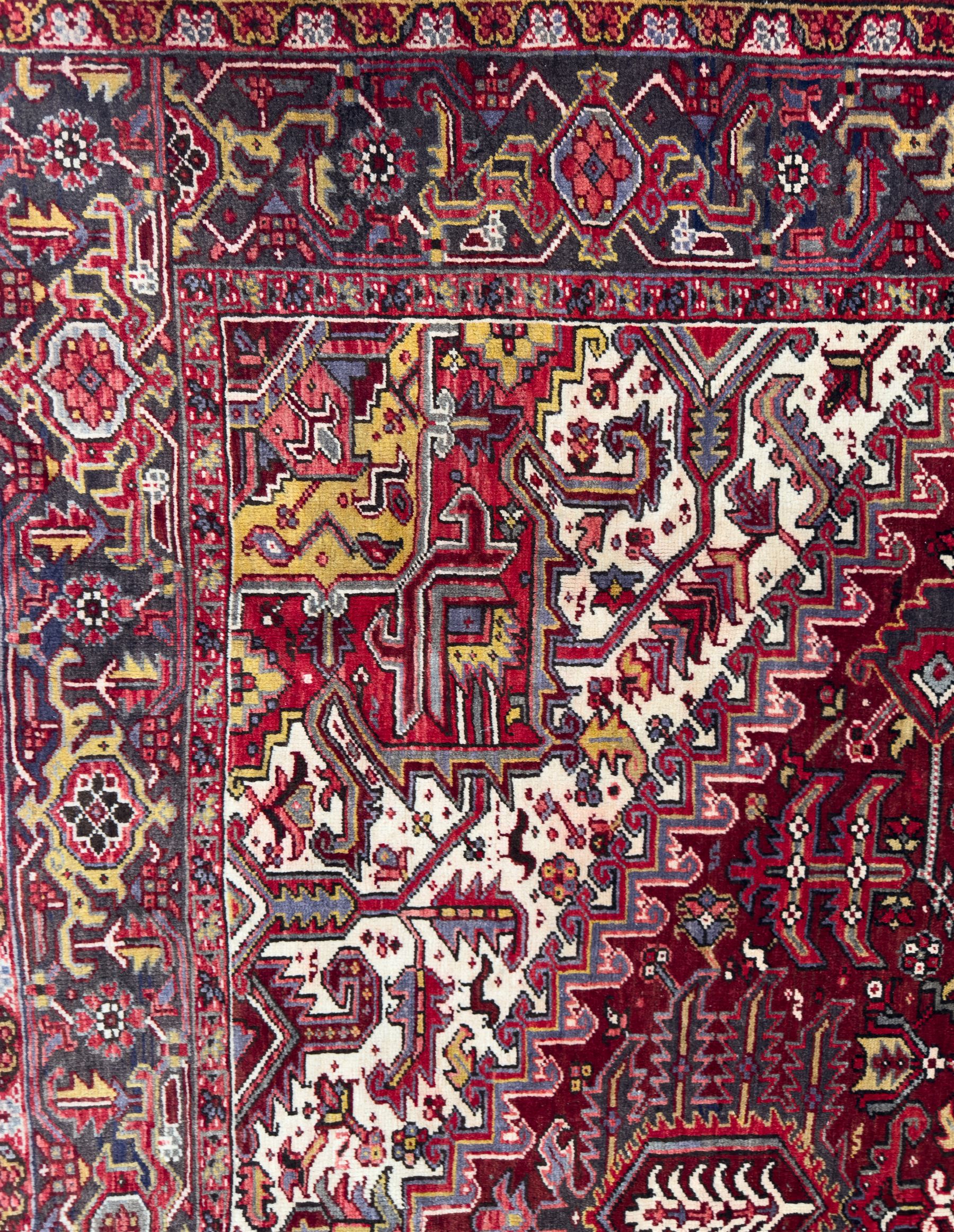 Northwestern Persian Heriz carpet, the madder red field centred by a large octofoil medallion with serrated edge, flanked by ivory stepped spandrels and geometric floral motifs in indigo, ochre and sky blue, enclosed by a navy border of rosettes and angular vines, from the region of Heriz