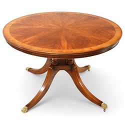 Regency design circular mahogany centre table, the radiating veneered top with contrasting crossbanded edge, on turned column support and four swept legs with brass paw feet and castors
