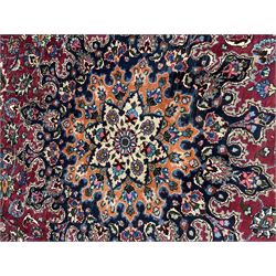 Persian Meshed carpet, plum ground and decorated with stylised flower heads and interlacing foliate, large central stylised medallion with orange detail, the orange mirrored in the five band border decorated with scrolling floral design, signature panel to end 