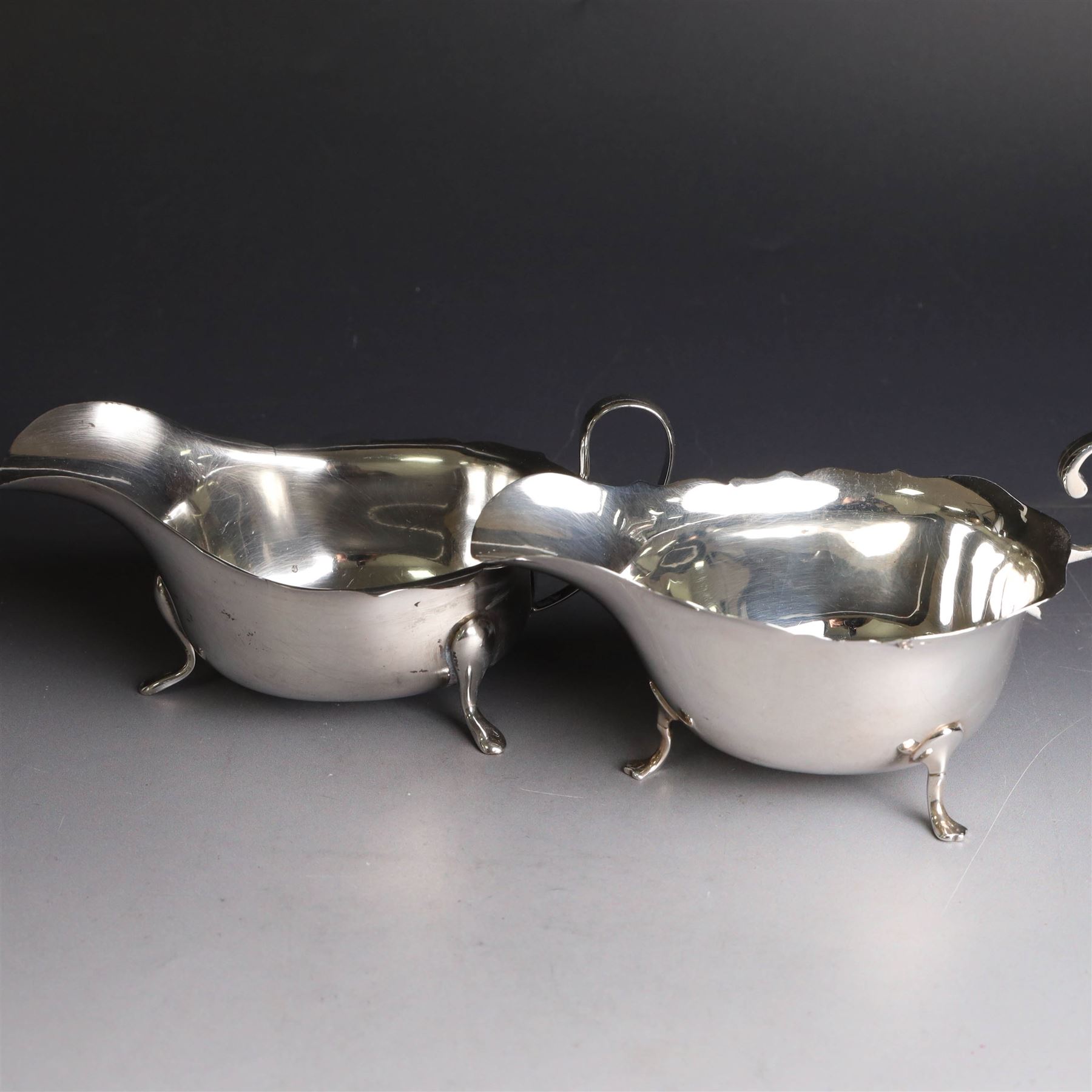 Three silver sauce boats, comprising pair of 1930s silver sauce boats, of typical form with shaped rim, scroll handle and upon three pad feet, hallmarked Viner's Ltd, Sheffield 1932 and a similar 1920s example with flying C scroll handle and upon three paw feet, hallmarked James Deakin & Sons, Sheffield 1923, tallest including handle H7.5cm