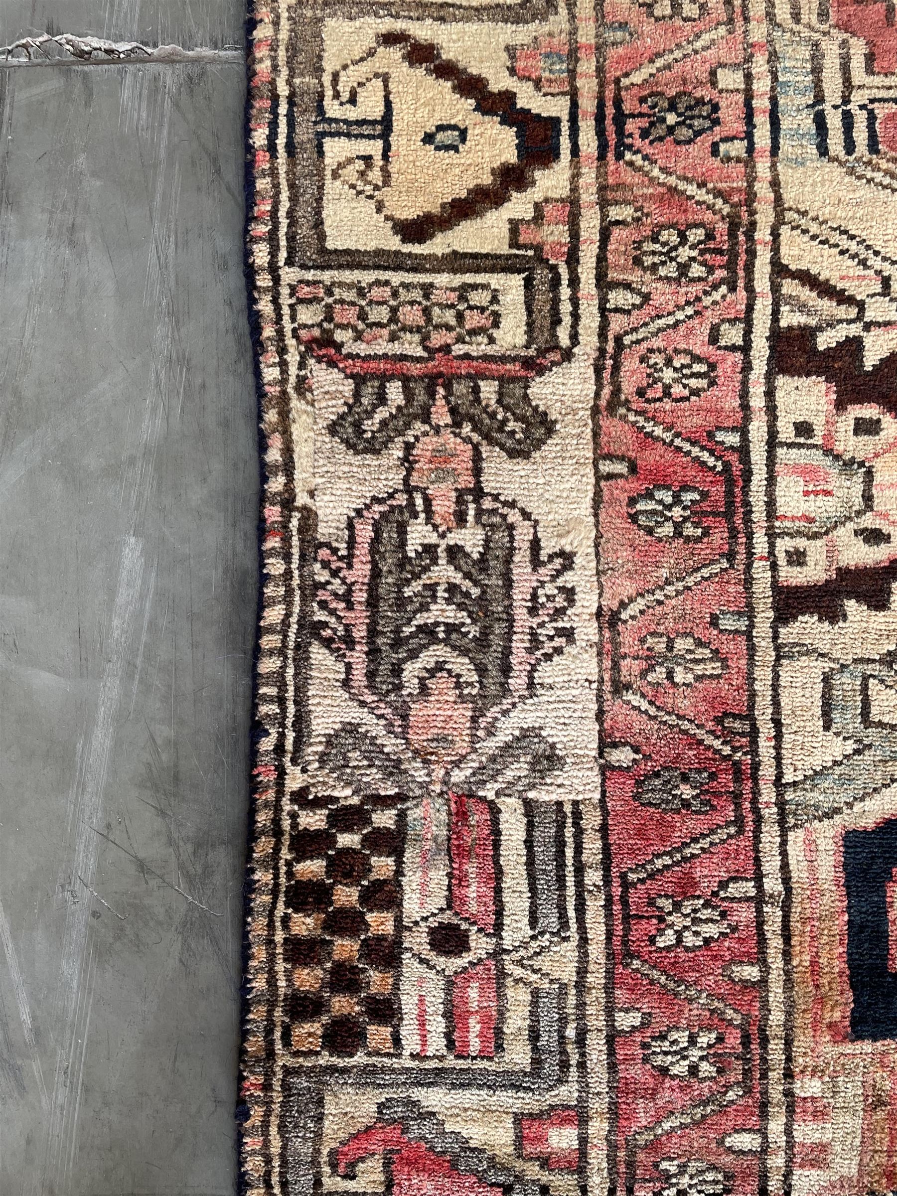 Persian Heriz red and pale ground rug, depicting multiple shaped panels with stylised motifs and designs, geometric patterned border