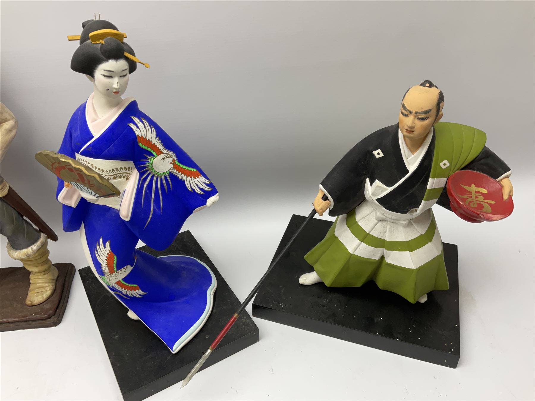 Clay Japanese Hakata dolls, comprising example modelled as a Geisha in blue kimono holding a fan, H41cm, another Geisha in pale pink kimono, H34cm, a Samurai, H35cm, and a composite figure of a Viking, H42.5cm. 