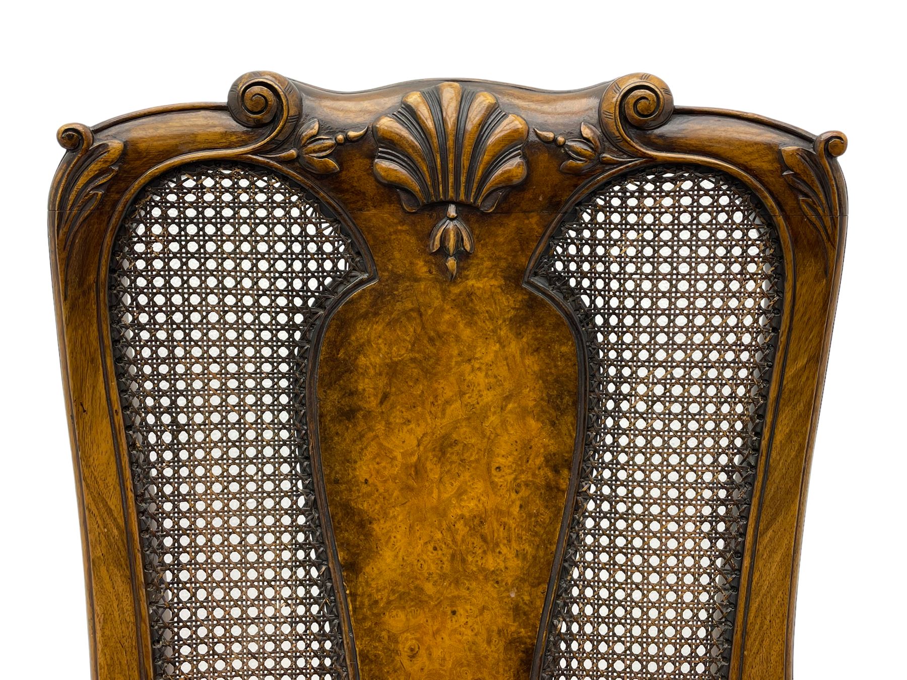 Pair of early 20th century Queen Anne design chairs, the cresting rail carved with scroll and central shell motif, shaped uprights and splat encased in cane work panels, shaped moulded seat frame with shell motif, floral needlework upholstered drop-in seat cushion, on shell carved cabriole supports with ball and claw feet, united by turned and shaped middle stretcher carved with acanthus leaf