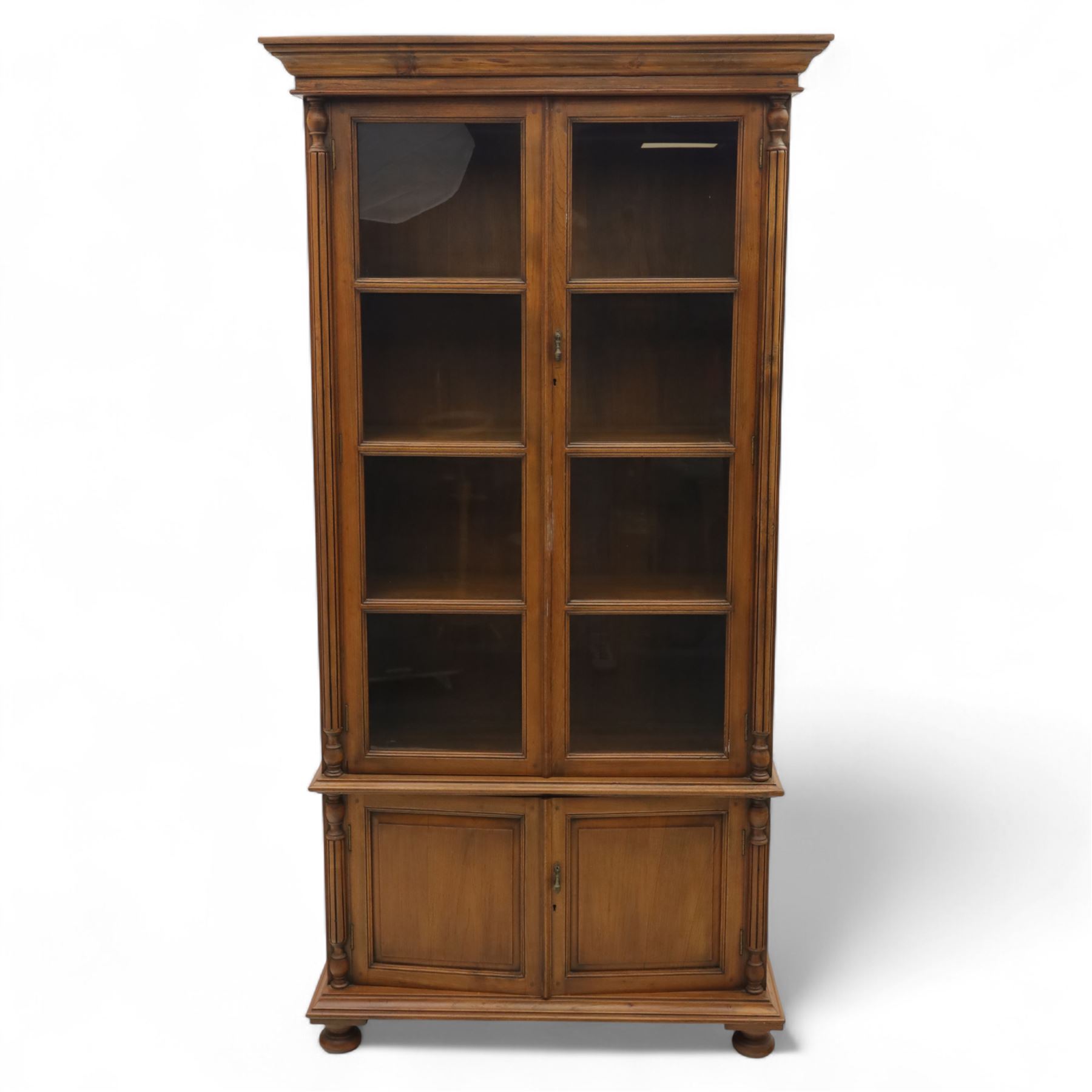 Pair of late 20th century Thai hardwood display cabinets, each with moulded cornice over twin glazed doors enclosing adjustable shelves, panelled cupboard doors below flanked by fluted columns, raised on bun feet