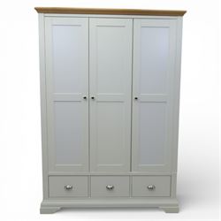 Modern triple wardrobe in white finish with oak moulded top enclosed by three doors with three drawers to base, with metal cup handles raised on bracket feet