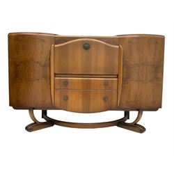Beautility - mid-20th century walnut sideboard, fall-front with sliding top enclosing mirror interior, fitted with two drawers and flanking cupboards, on sledge feet with curved stretchers 