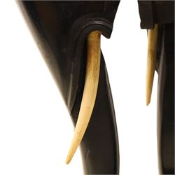 Oriental design black lacquered jardinière stand, circular moulded top with raised rim, the base formed as three elephant heads with carved ears and simulated tusks, on shaped supports with paw terminals