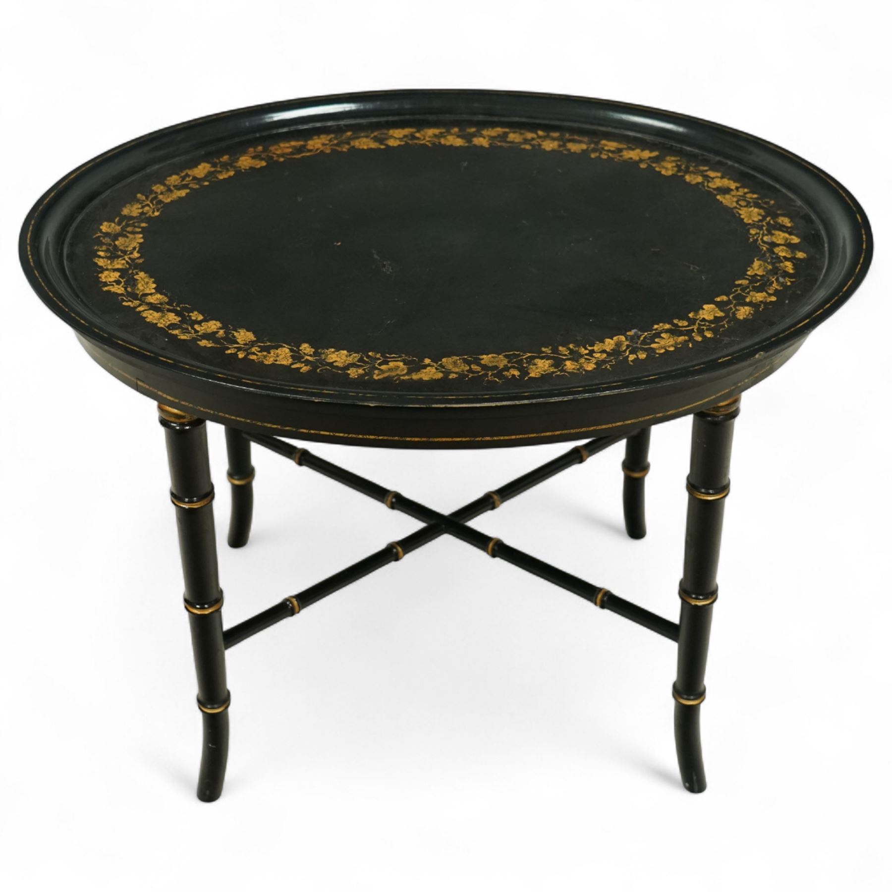 Regency style oval toleware tray table, the black lacquered top with gilt floral decoration, on ebonised faux bamboo frame with stretcher supports