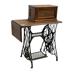 Singer - early 20th century cast iron treadle sewing machine, with hand crank wheel and oak work surface, the machine decorated with gilt foliate detail, complete with rectangular wooden cover and folding extension leaf