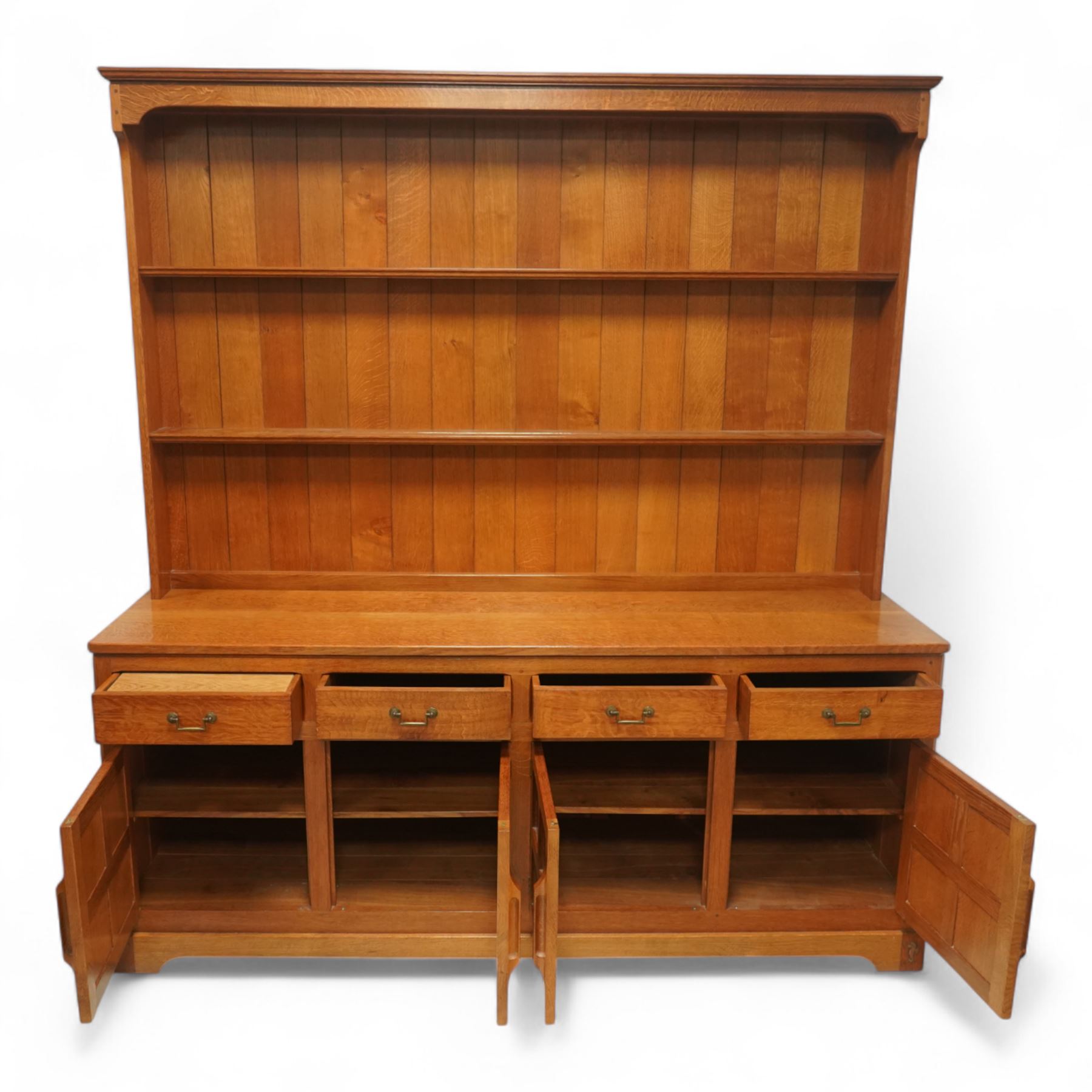 Seahorseman by Shaw & Riley - Yorkshire oak Welsh dresser, the dresser rack of rectilinear form with plain frieze and projecting moulded edge above two shelves with central shallow groove, the base section fitted with four drawers and a fitted cutlery drawer containing cutlery, above four panelled cupboard doors with geometric mouldings and carved sculpted handles, interior with single shelf and sides with geometric mouldings raised on a shallow plinth base with shaped bracket feet, with signature Seahorse carving from the workshop from the workshop of A. Shaw & Riley Ltd, Hessay