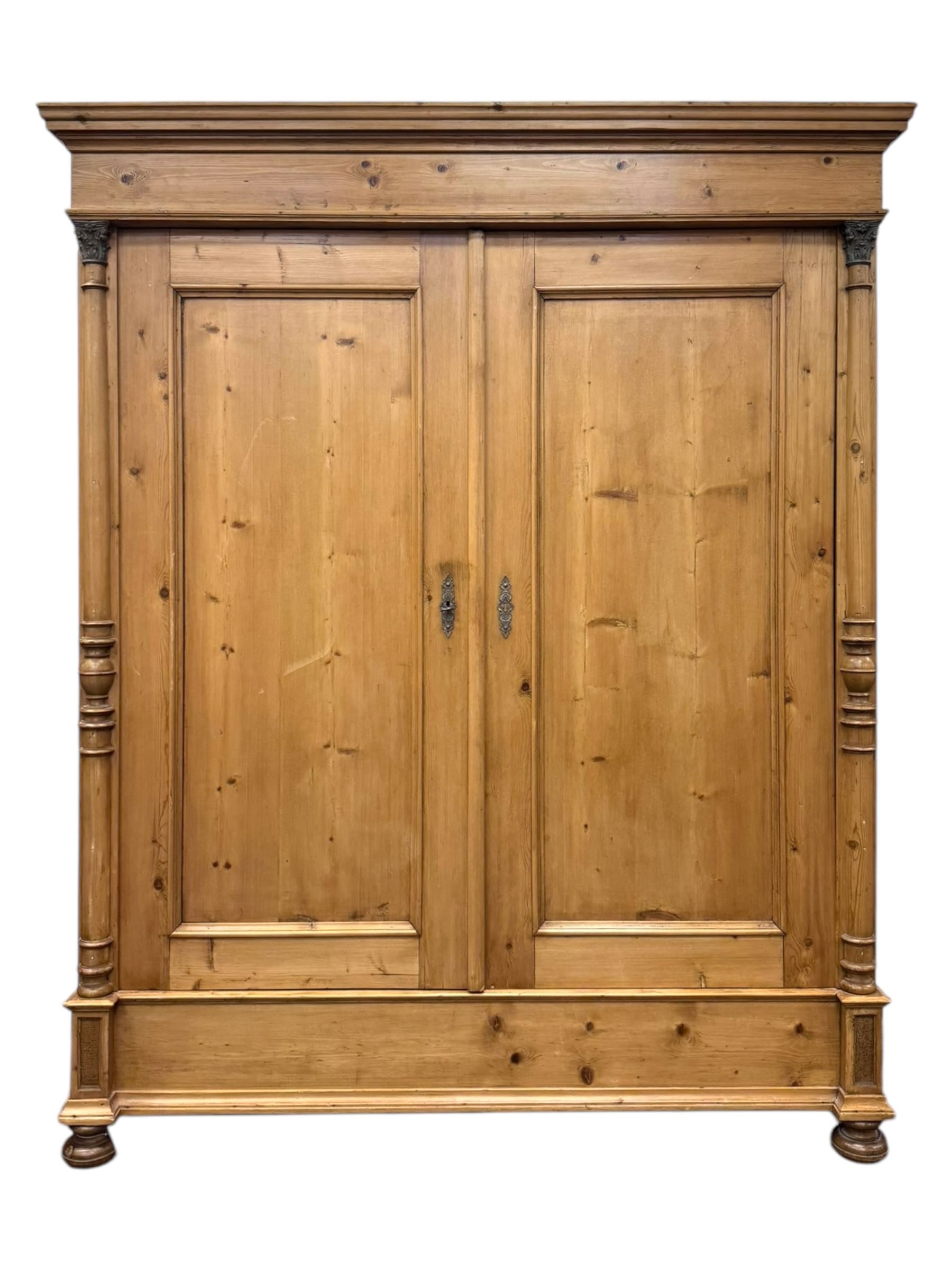 Large 19th-century Continental polished pine double wardrobe, panelled back and doors revealing brass hanging rod, flanked by half-turned columns with Corinthian capitals supported on bun feet