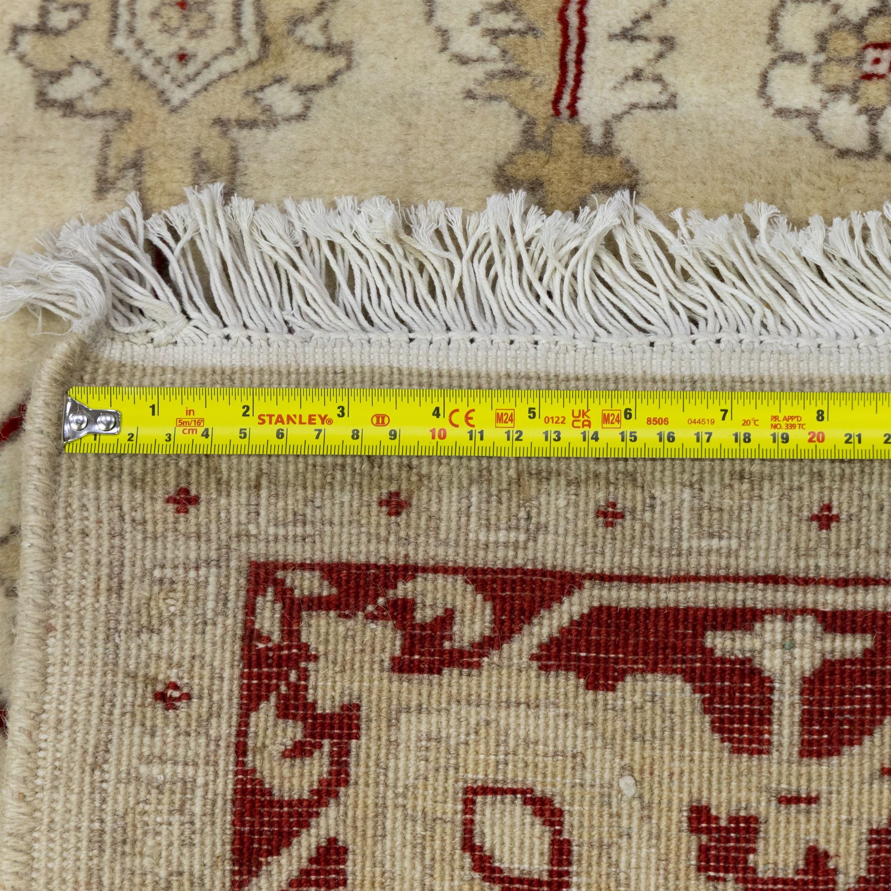 Baluchi signed hand-knotted rug, ivory ground, with an all-over geometric lattice design incorporating stylised flowerheads, hooked motifs and angular vine work, enclosed by a crimson border with repeating floral motifs and scrolling vines, flanked by narrow patterned guard stripes, signed to one corner, with cotton fringes