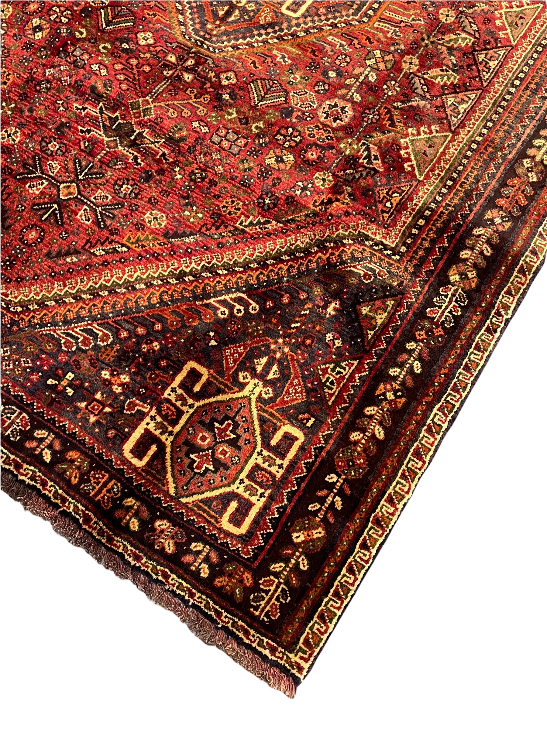 Persian Qashqai red ground rug, the main field decorated profusely with small stylised motifs, central lozenge medallion, multi-band border decorated with trailing foliate and flower head motifs 