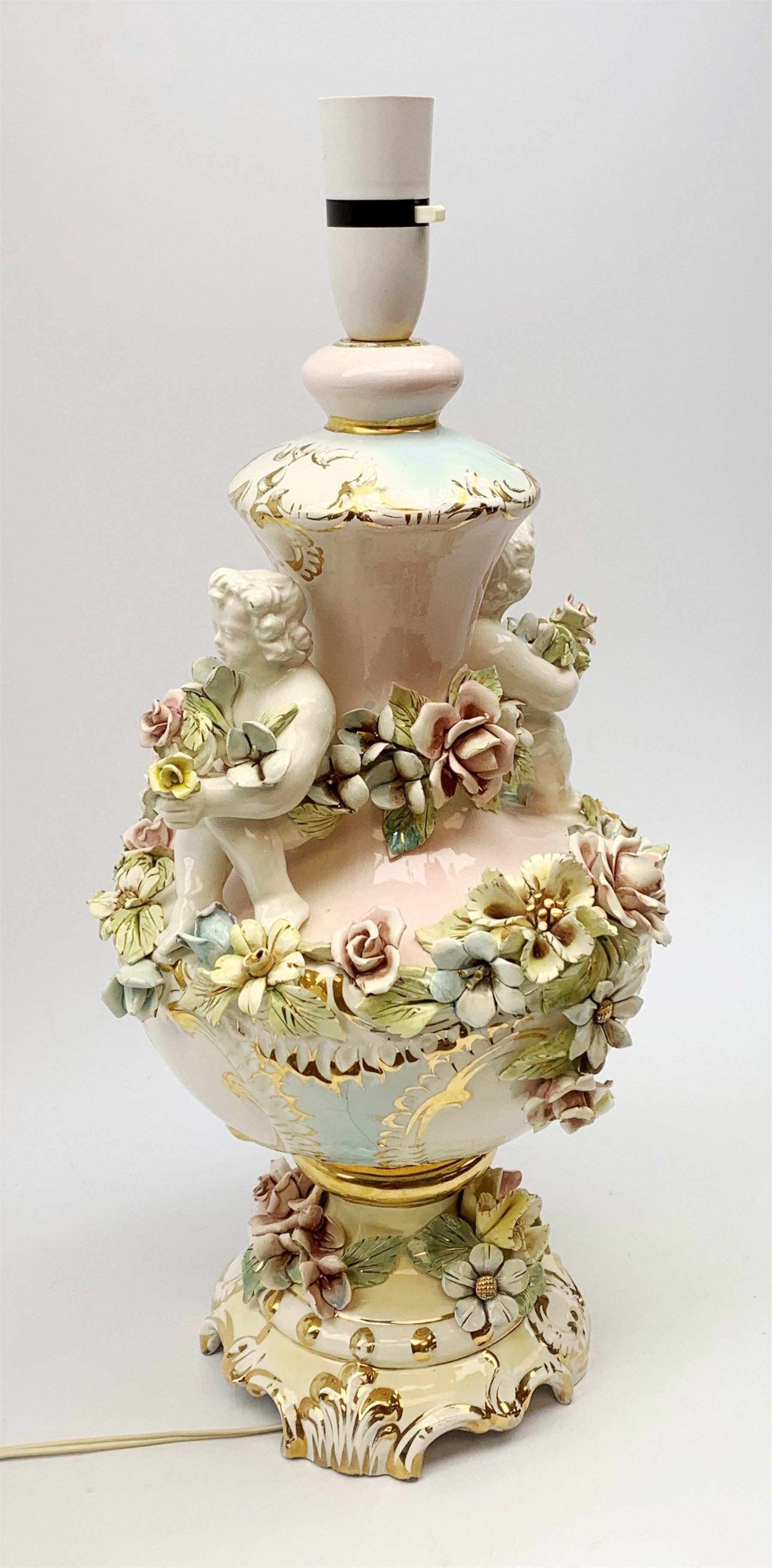 An Italian Capodimonte style lamp base, of pedestal urn form with applied putti and encrusted flower detail, heightened with gilt, overall H46cm. 