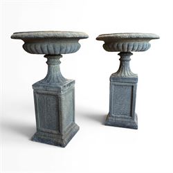 Pair of cast stone garden urns of kylix form on pedestals, the broad egg-and-dart moulded rim over a shallow gadrooned underbelly, with waisted tapering base, raised on matching plinth bases with faux panelled facia