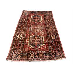 Persian Heriz red ground rug, the field decorated with three medallions, decorated all over with stylised and geometric motifs, triple band border 