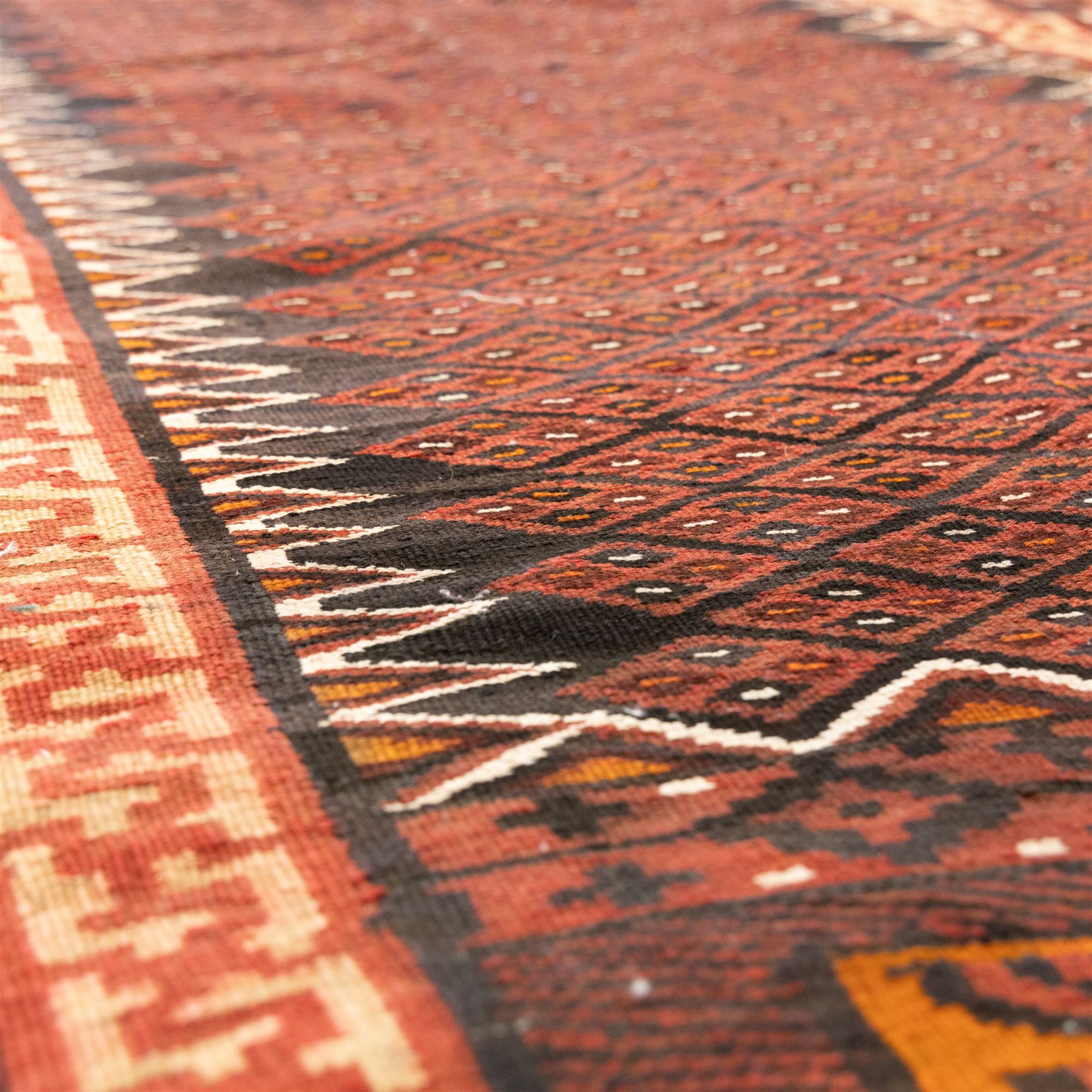 North west Persian Yamut Kilim, madder field with all-over lozenge lattice and serrated edges, with stepped end-panels and bold geometric borders in red, ivory and black