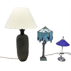 Three table lamps, comprising a blue example upon Corinthian column with leaded blue shade, chrome example with frosted dark blue shade and large  example decorated with geometrc pattern with cream fabric shade