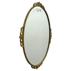 Oval gilt wall mirror, with bevelled edge plate within a moulded frame cast with acanthus scrolls and foliate decoration, pierced cartouche crest and apron, flanked by scrollwork handles