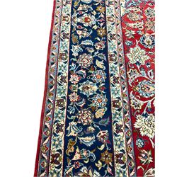 Large Persian Kashan carpet, the red ground field decorated with floral central medallion and spandrels, overall floral design depicting trailing branches with stylised plant motifs, guarded blue ground border with stylised flower head motifs