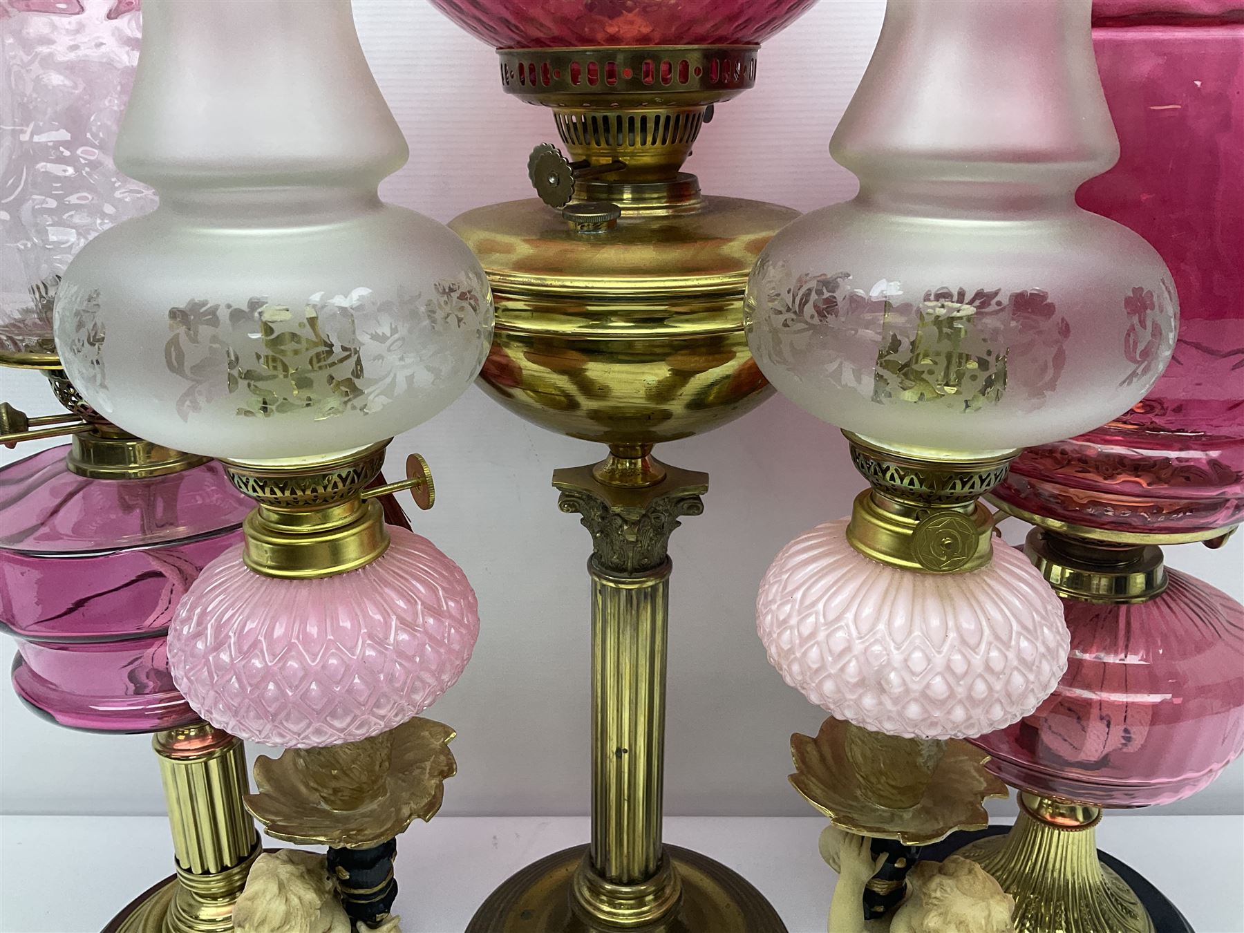 Victorian cast brass oil lamp, with fluted pink glass shade, together with two smaller brass oil lamps with pink shades and reservoirs and a pair of oil lamps, the bases modelled as putti, with pink glass reservoir  and frosted shades, tallest H70cm