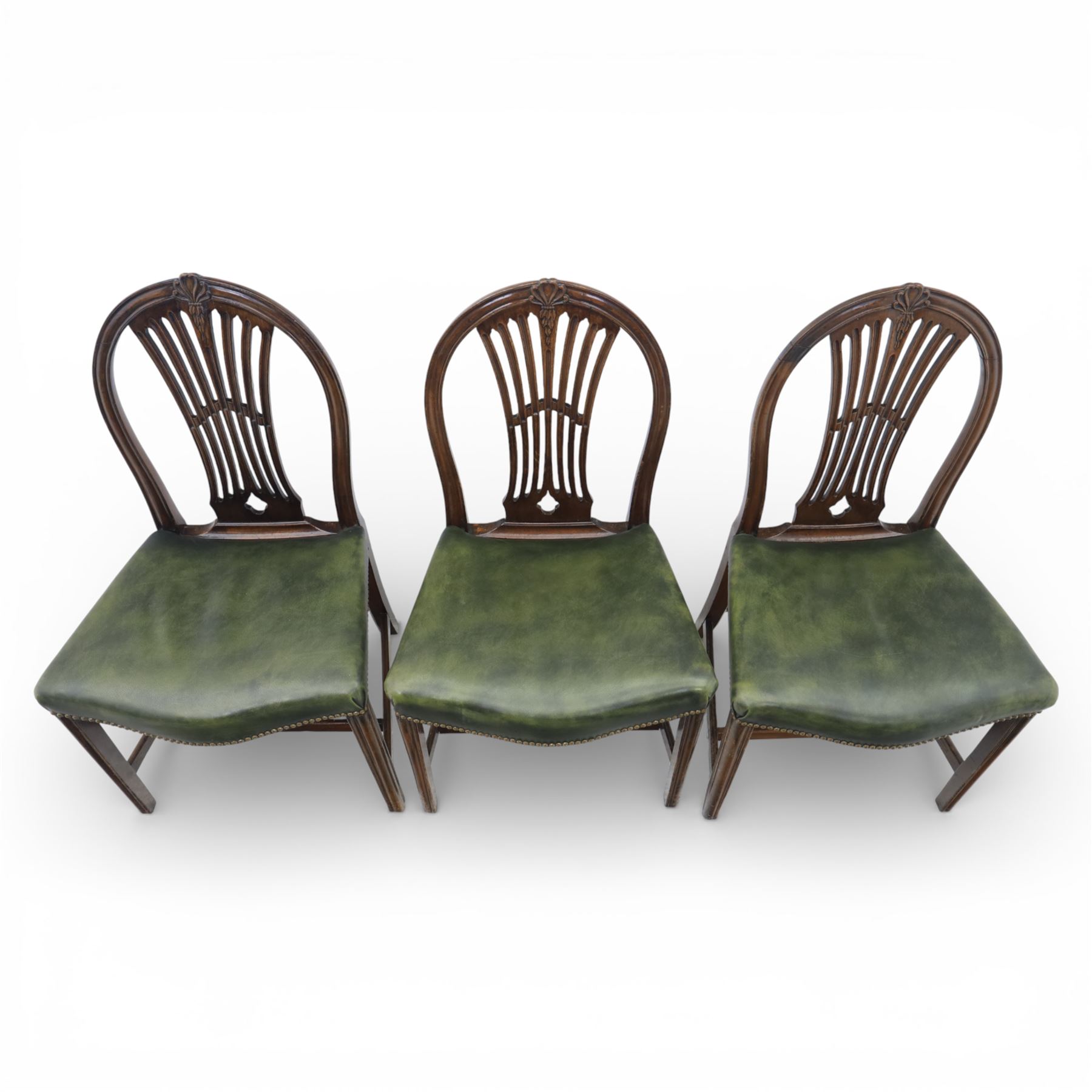 George III style set of six mahogany dining chairs, the arched backs with pierced and carved vase splats beneath carved husk and patera detail, drop-in upholstered seats covered in green leather with brass studded edging, raised on square section legs united by plain stretchers