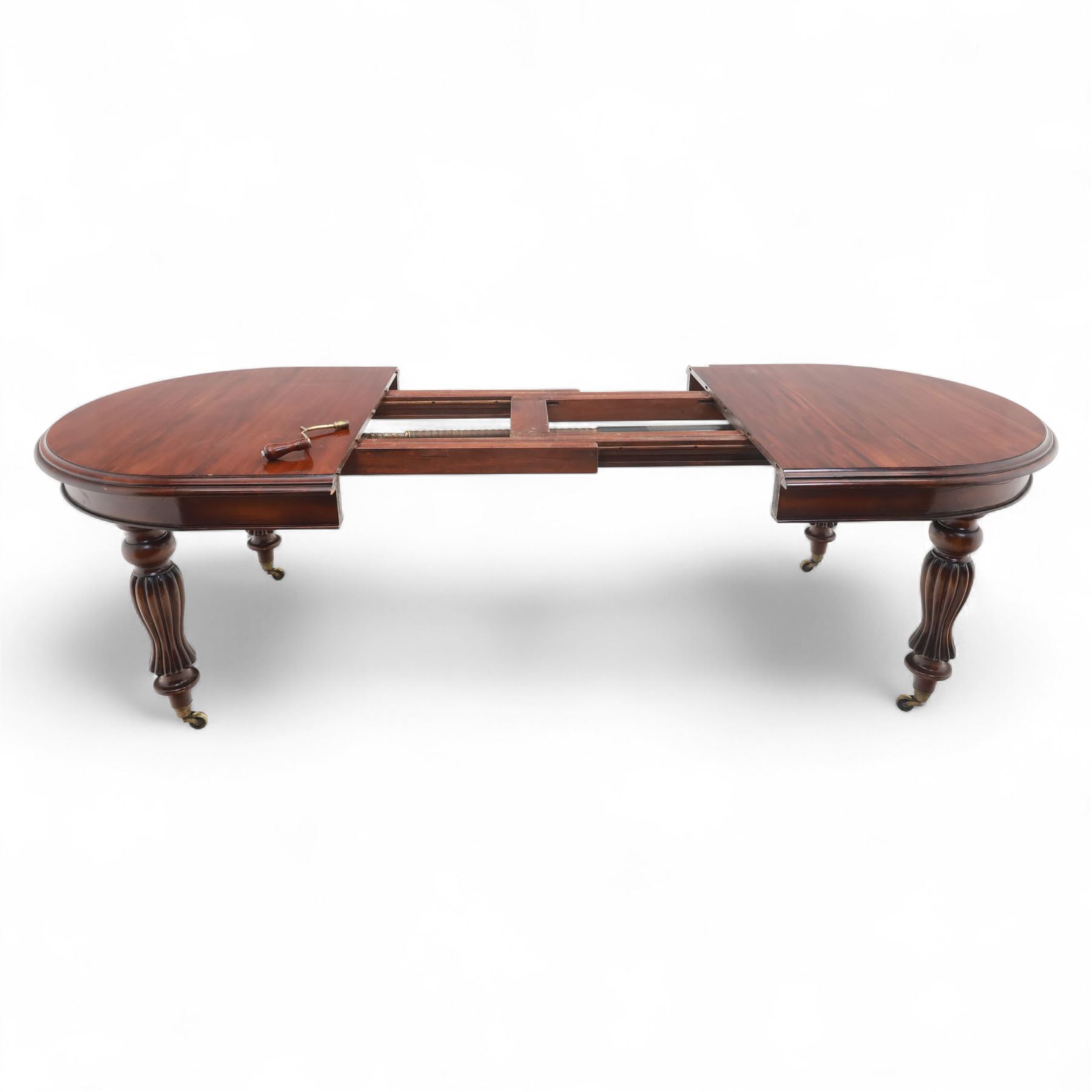 Victorian mahogany extending dining table, rounded rectangular top with moulded edge, pull-out action fitted with two additional leaves, raised on four reeded and fluted baluster legs with brass caps and castors