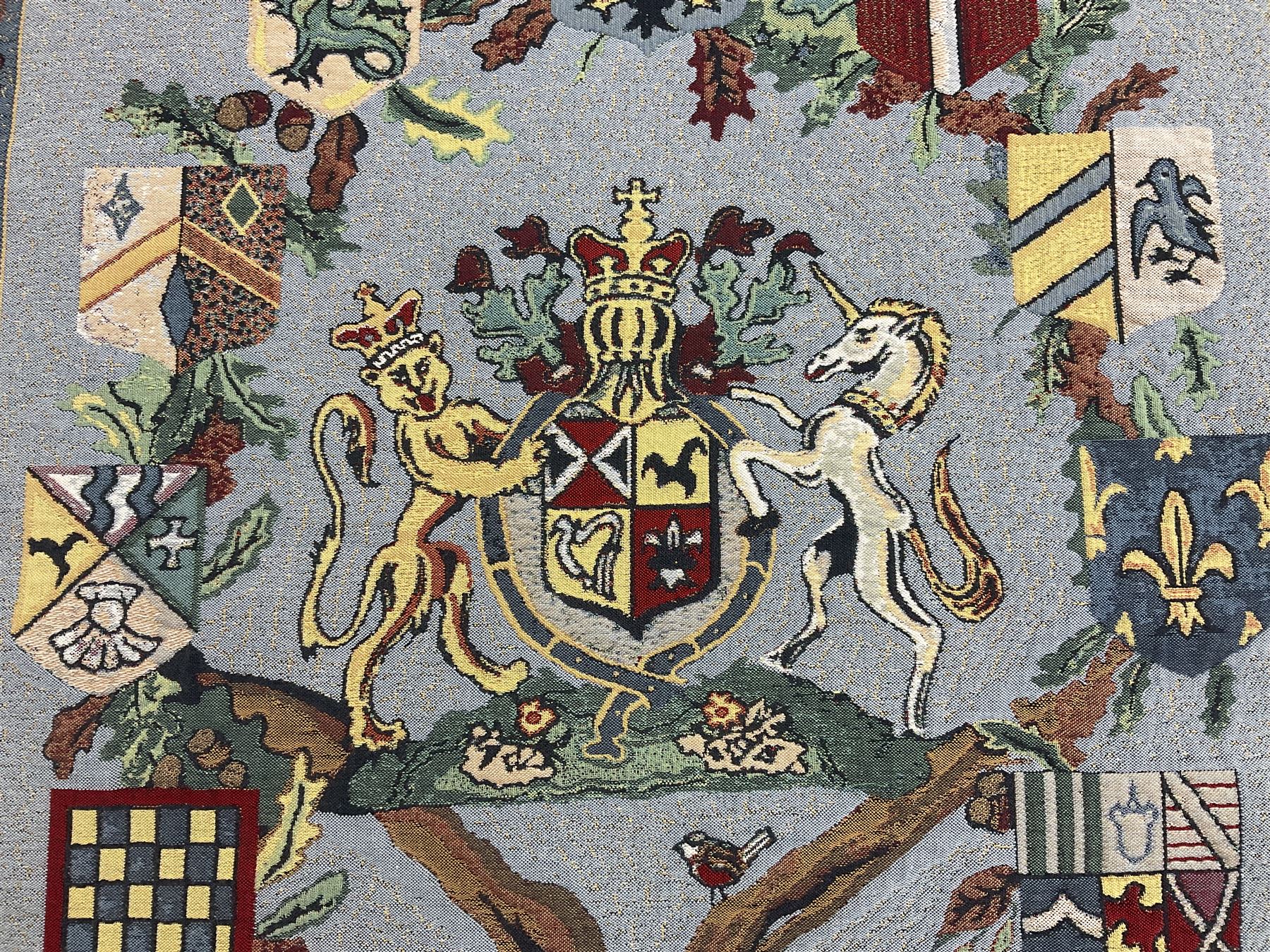 Three tapestries comprising 20th century wool tapestry panel of a medieval nobleman upon a horse with a castle in the distance, together with a smaller tapestry depicting The English Coat of Arms, both hung on rails, and further depicting village scene, largest approx 132cm x 95cm