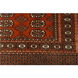 Bokhara hand-knotted carpet, terracotta ground with repeating rows of Tekke guls interspersed with geometric motifs, enclosed by multiple stylised floral and geometric borders, with fringed ends
