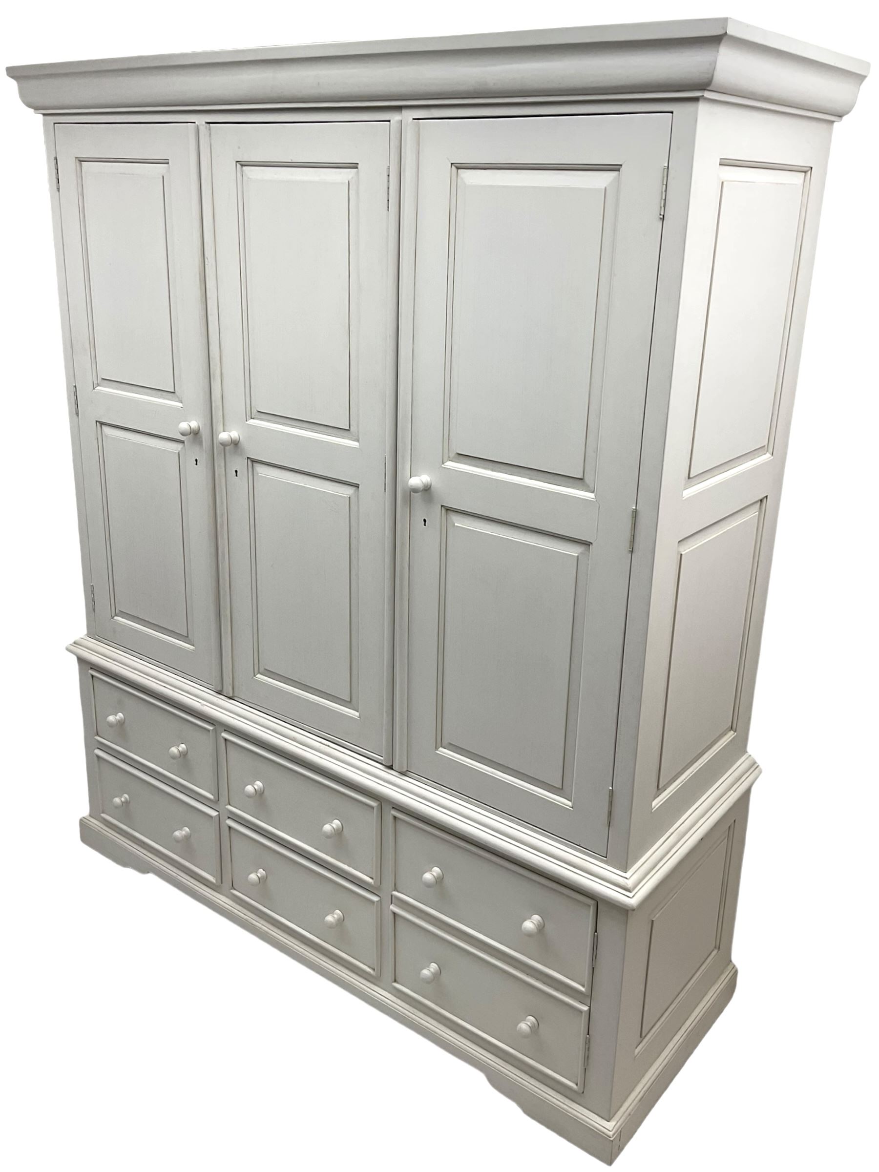 White painted triple wardrobe, projecting moulded cornice over three panelled doors, the interior fitted with hanging rails, four drawers and hinged cupboard to base, on bracket feet