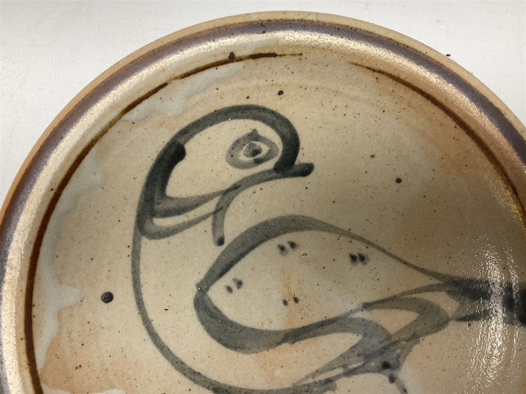 Studio pottery bowl, probably by Svend Bayer of Wenford Bridge, the stoneware body of shallow circular footed form with brushwork decoration of a stylised bird figure in grey upon peach ground within bands of iron red, unmarked, D18.5cm