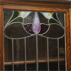 Arts and Crafts oak dresser, projecting moulded cornice above three glazed panels with coloured leaded glass floral panels, flanked by two glazed doors enclosing two adjustable shelves, open mirrored recess below with mirrored back, the base fitted with two short drawers over two central drawers flanked by carved panelled cupboard doors, ornate brass handles, raised on tapering square legs