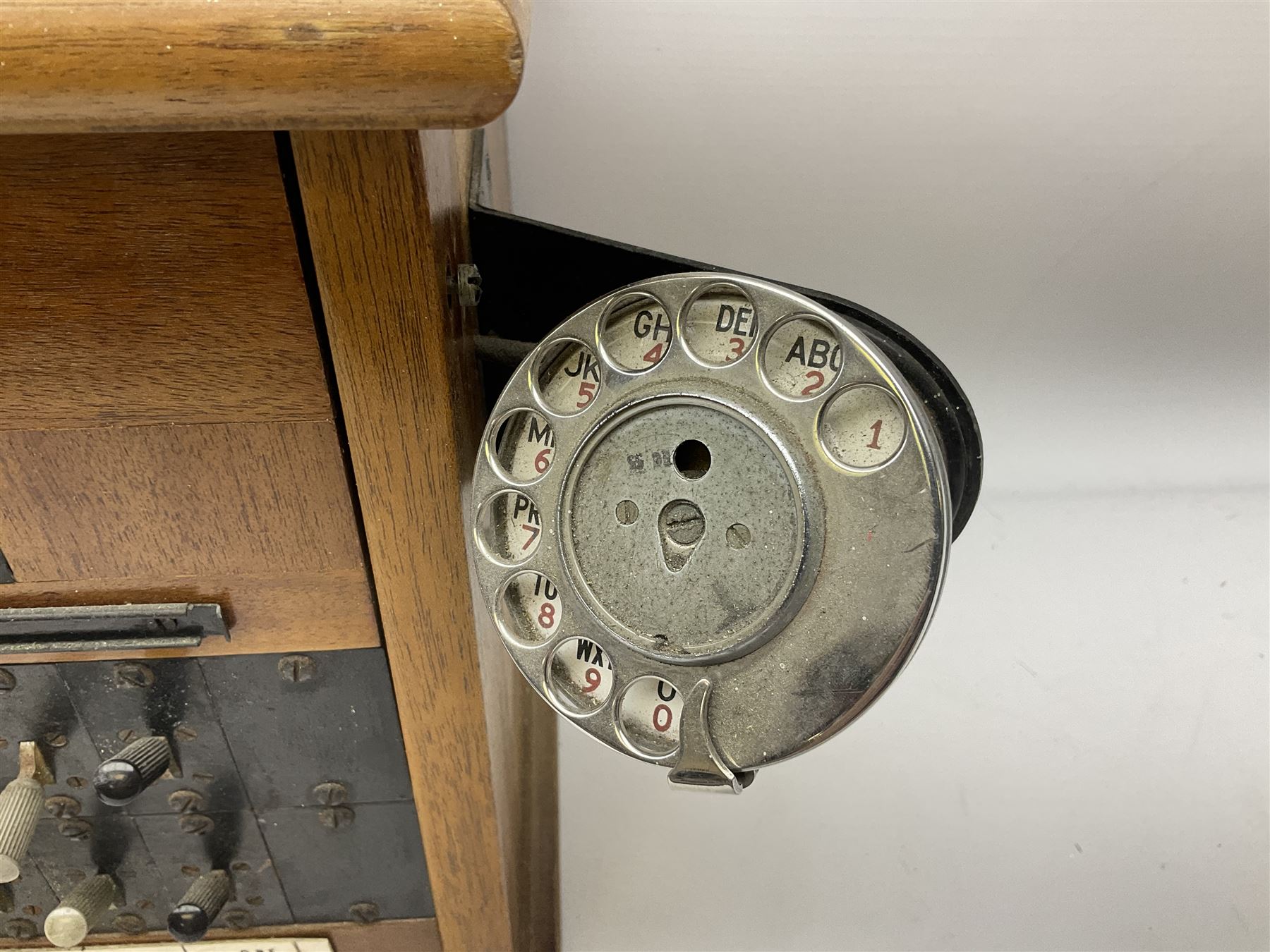 Early-mid 20th century internal telephone system, comprising exchange box with attached TMC rotary telephone and dictograph with Bakelite handset and support upon stained wood case, and 1960s black Bakelite telephone model 312L with G.P.O sticker beneath, largest H30.5cm W36.5cm D30cm