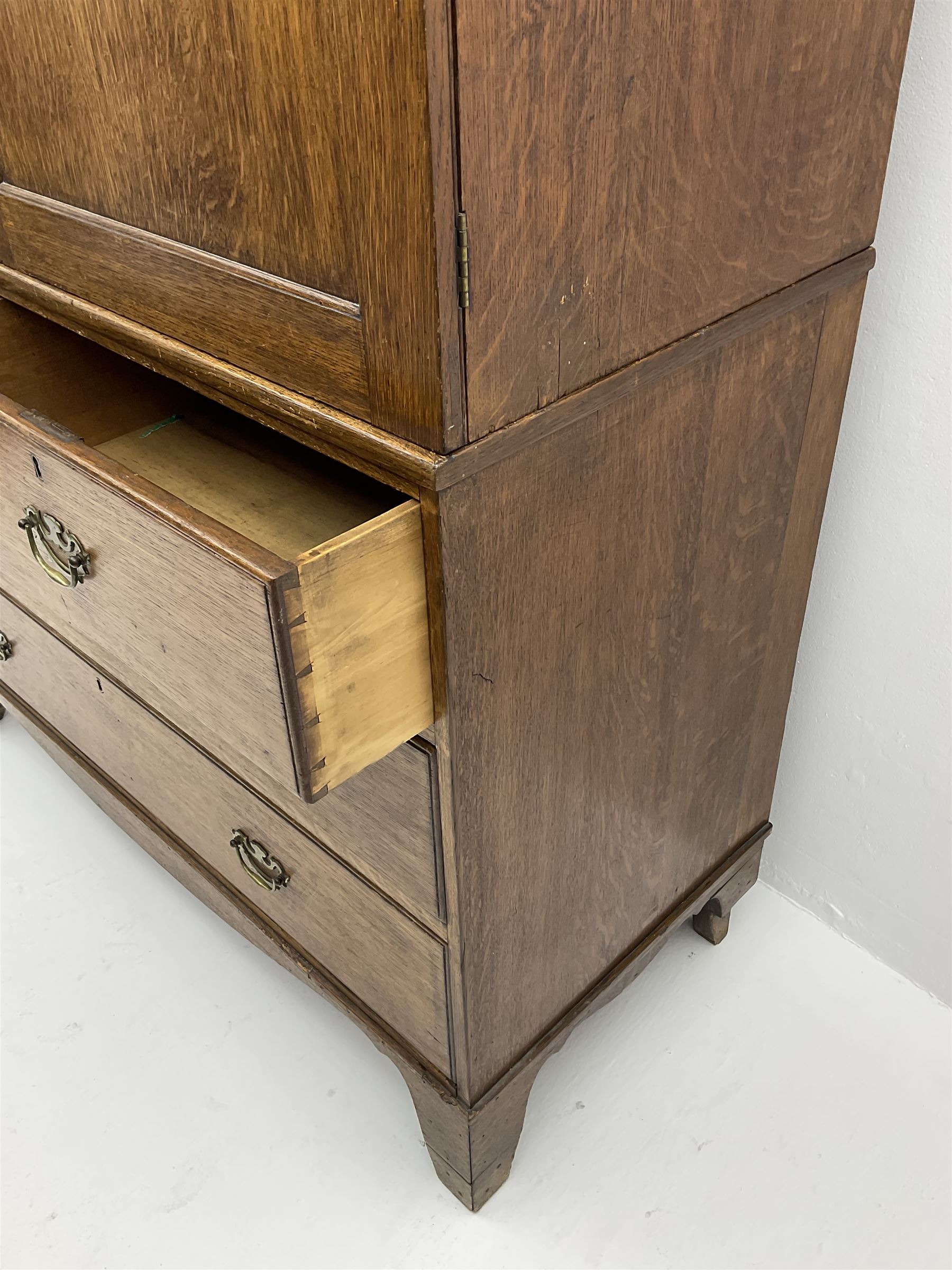 Early 19th century oak linen press cupboard, the projecting cornice over two panelled doors enclosing shelves, two short and two long drawers below, bracket feet