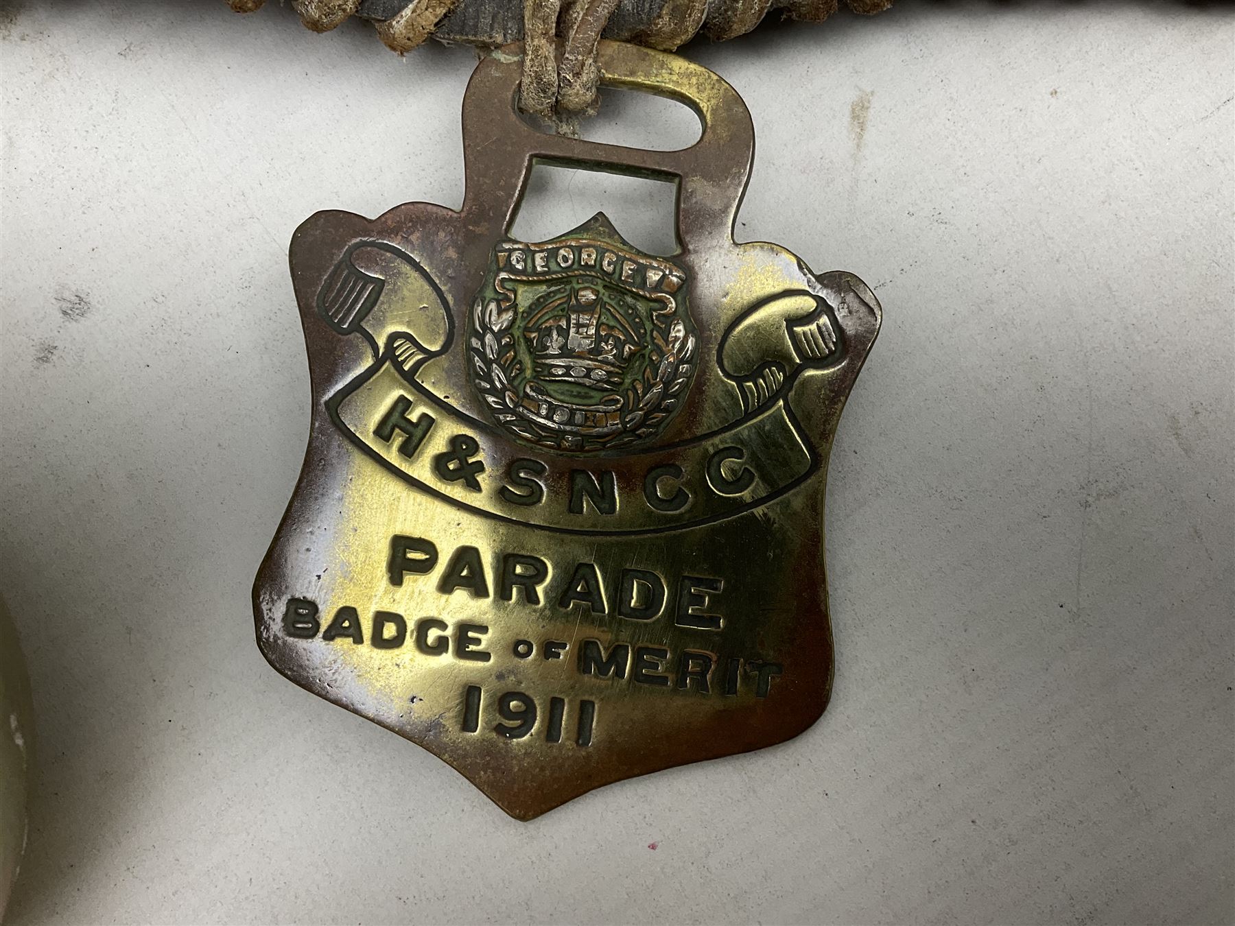 Victorian Queen Victoria record reign horse brass and H&SNCC Parade Badge of Merit 1911 horse brass, both on leather strap, together with 1924 British Empire Exhibition brass Lipton's souvenir tea caddy, strap L36cm