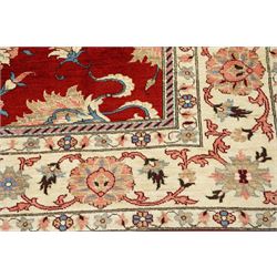 West Persian Sarough hand-knotted carpet, rich madder red field, decorated with stylized palmettes angular vinery and floral sprays within multiple borders of ivory ground and scrolling foliate decoration, with cotton fringe ends 