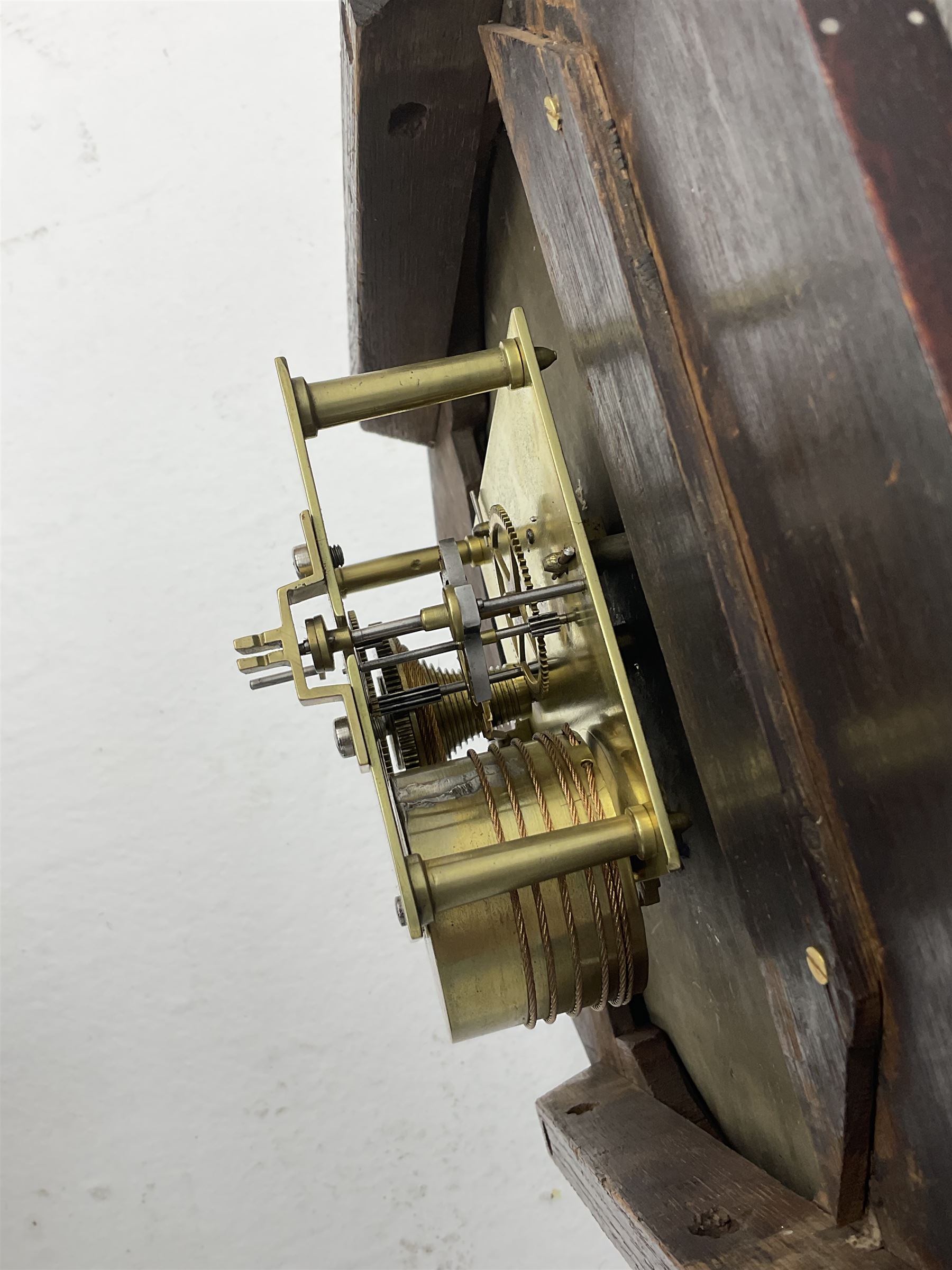 Mid-19th century mahogany veneered eight-day four-pillar single fusee drop dial wall clock with an octagonal dial surround and scroll brass inlay, circular painted steel dial with roman numerals and minute track, matching trefoil steel hands, brass bezel with a flat glass, curved trunk with brass inlaid circles and stringing around the glass pendulum aperture with a brass slip, carved ear pieces in the form of flowers and leaves, with pendulum adjustment door and movement door. With Pendulum & Key