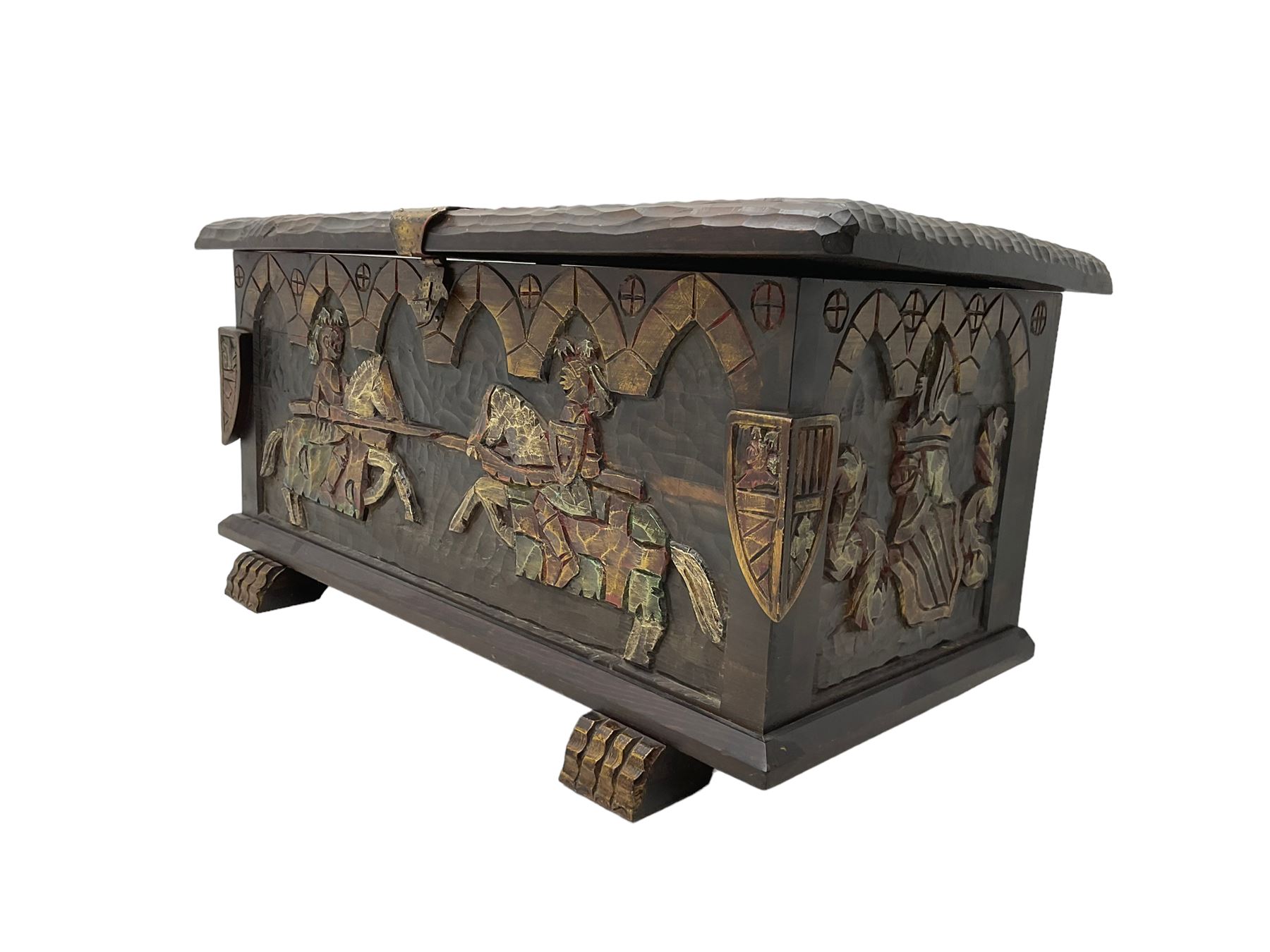 Carved wooden blanket chest, the tooled hinged lid with shaped metal strap hinges and catch, the front carved with arcade over two medieval jousters, on carved sledge feet
