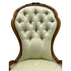 Victorian walnut framed nursing chair, the cresting rail decorated with carved applied flower heads and acanthus leaves, shaped back and sprung seat upholstered in buttoned ivory damask fabric, serpentine front over cartouche carved cabriole supports with ceramic castors (W57cm H92cm); with matched footstool, circular top over shaped moulded apron, on floral carved cabriole feet (W34cm) 