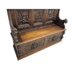 19th century heavily carved oak settle, the moulded upper rail over triangular foliage carved frieze, three Flemish style carved panels depicting tavern scenes, acanthus carved uprights terminating to lion carved arms, hinged box seat, the panelled front carved with lion masks and extending scrolled acanthus leaves, on moulded skirt base