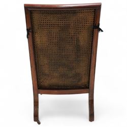 George IV mahogany framed library reading chair, reed moulded frame with cane work seat, back and sides, with loose cushions upholstered in green buttoned leather, upholstered arm rests, turned arm supports terminating to turned and reed carved feet, on castors 