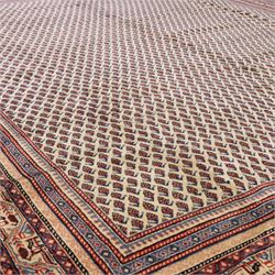 North West Persian Boteh-Mir hand-knotted rug, madder red field decorated with an all-over lattice of small boteh motifs and a central stepped lozenge medallion with repeating stylized boteh and geometric devices, spandrels similarly worked, with multiple narrow borders of floral and geometric bands, in tones of madder red, indigo blue, ivory, and soft green, with cotton fringe ends