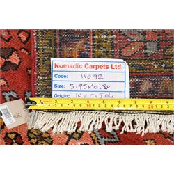 North West Persian Karajeh hand-knotted runner, madder red field with a series of shaped hexagonal medallions and cruciform motifs each enclosing geometric rosette devices linked by angular vine elements, field populated with stylized tribal ornaments, within narrow multiple borders decorated with repeating angular motifs framed by guard stripes of geometric devices, with cotton fringe ends  