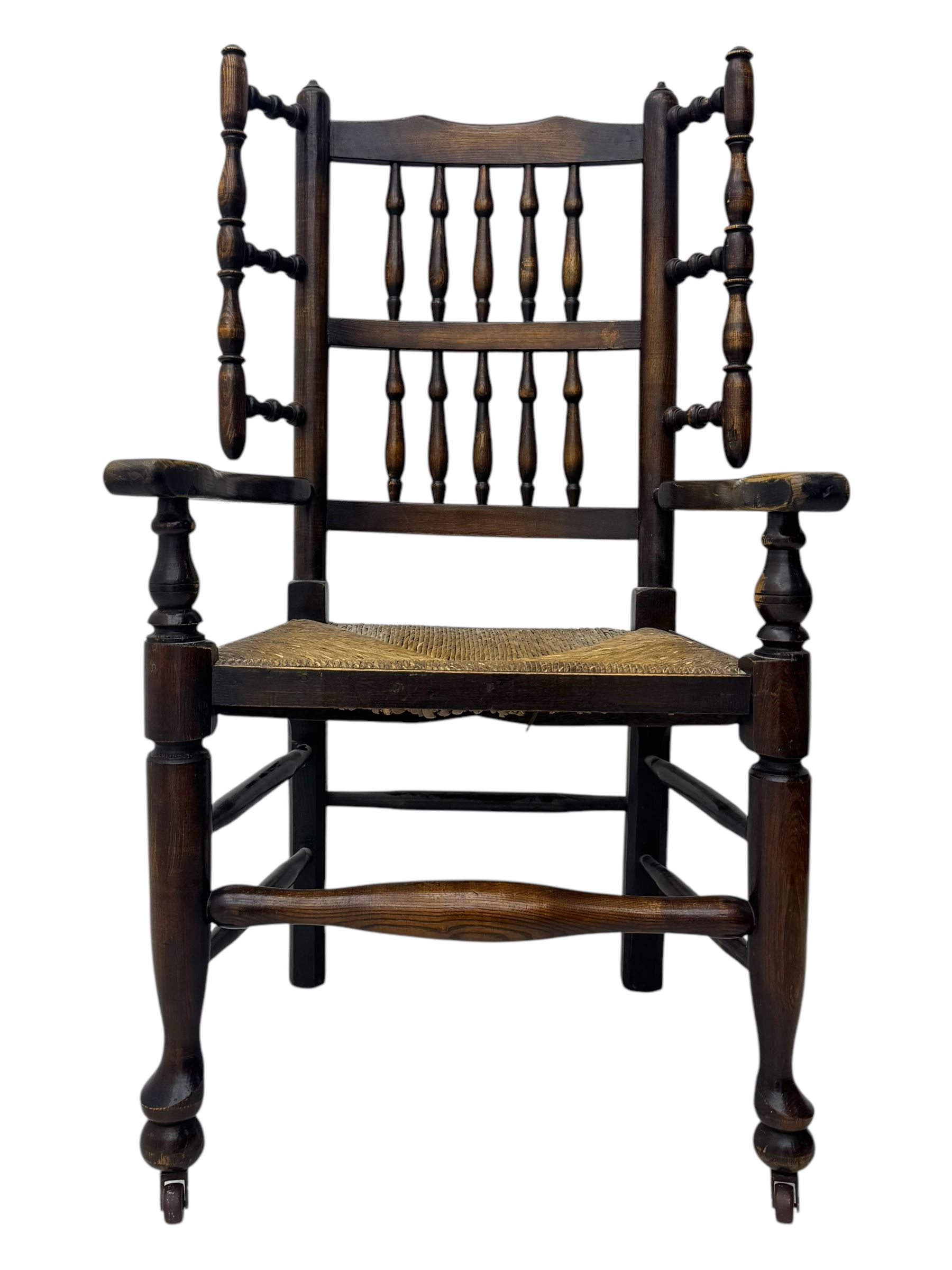 Early 19th century ash armchair, the back with winged spindles extending from a shaped top rail, above a splat of two rows of vertical spindles, with curved arms and a rush seat, raised on turned supports united by double stretchers terminating in castors