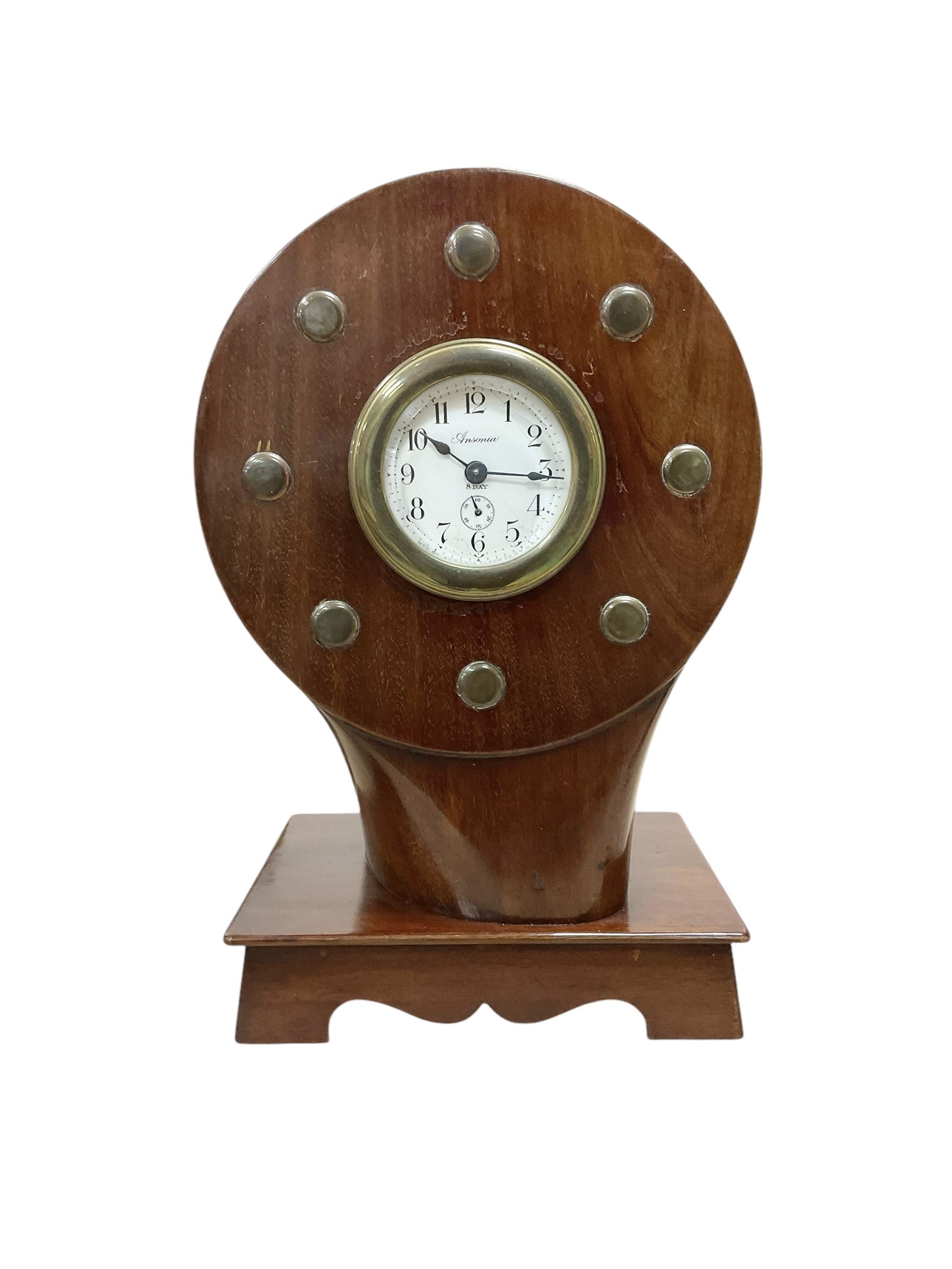 1920's-Aviation clock, mahogany case configured from part of an early 20th century aeroplane propellor, mounted on a conforming plinth with a shaped base, bolt holes filled with brass studs and fitted with an 8-day American spring driven Ansonia insertion movement with a porcelain dial, Arabic numerals, spade hands and seconds dial. Wound and set from the rear.