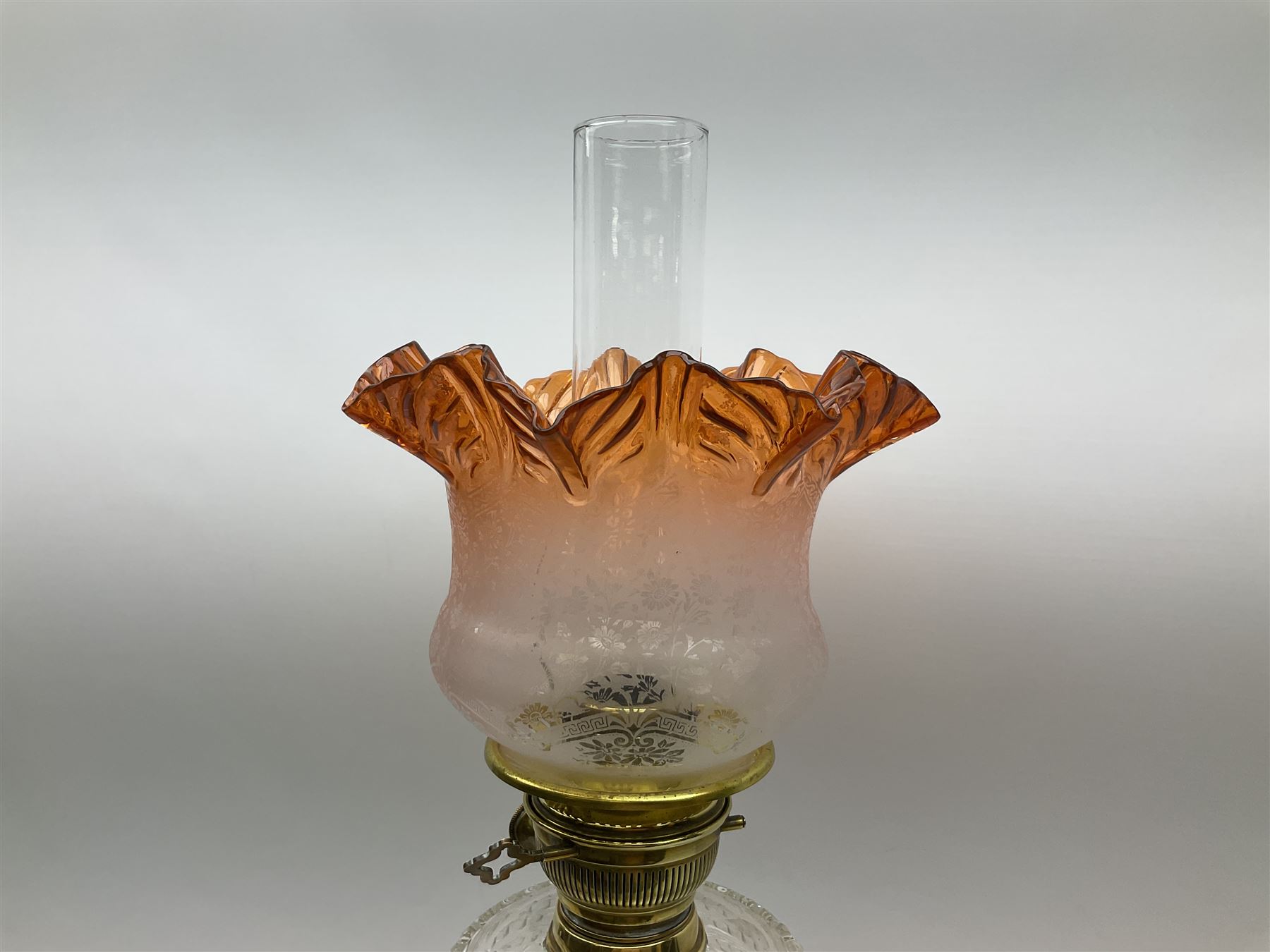 Victorian brass oil lamp, the square stepped base leading to a Corinthian column supporting a part slice cut clear glass reservoir, burner, clear glass chimney and foliate etched glass shade with amber rim, overall H80cm