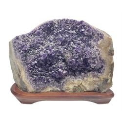 large amethyst crystal geode cluster, with well-defined crystals of various sizes, upon a carved wooden stand 